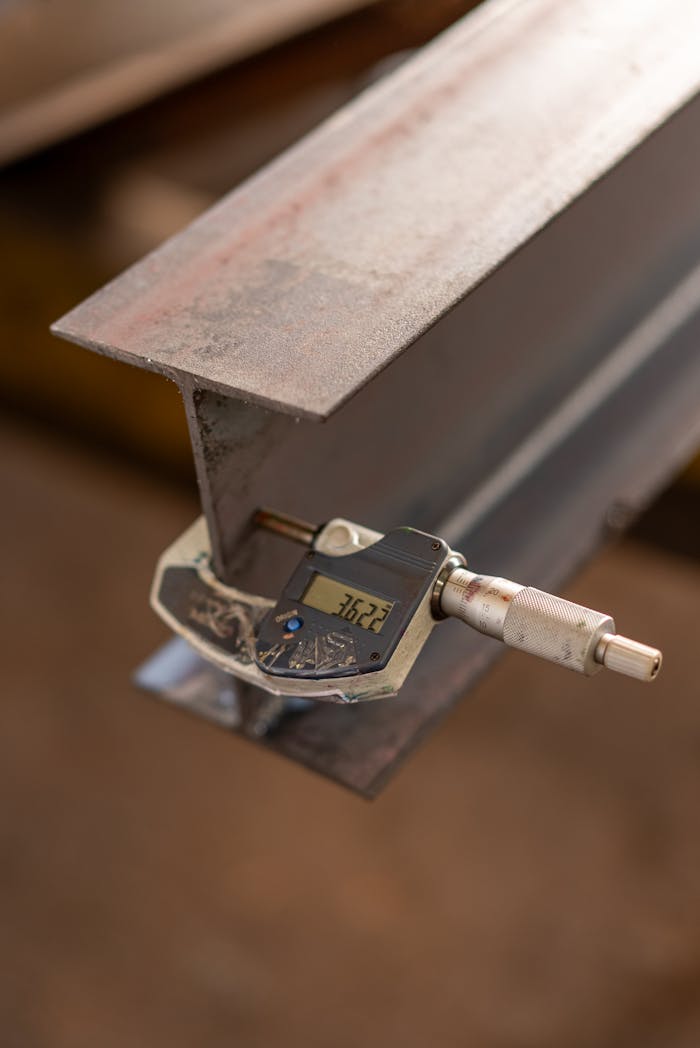 Close-up of an industrial caliper measuring the thickness of a steel beam in a workshop.